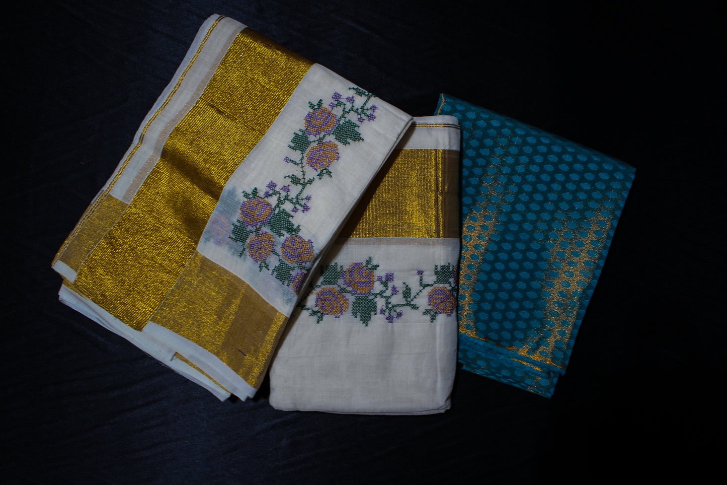 Three embroidered towels in gold, white, and blue on a dark surface