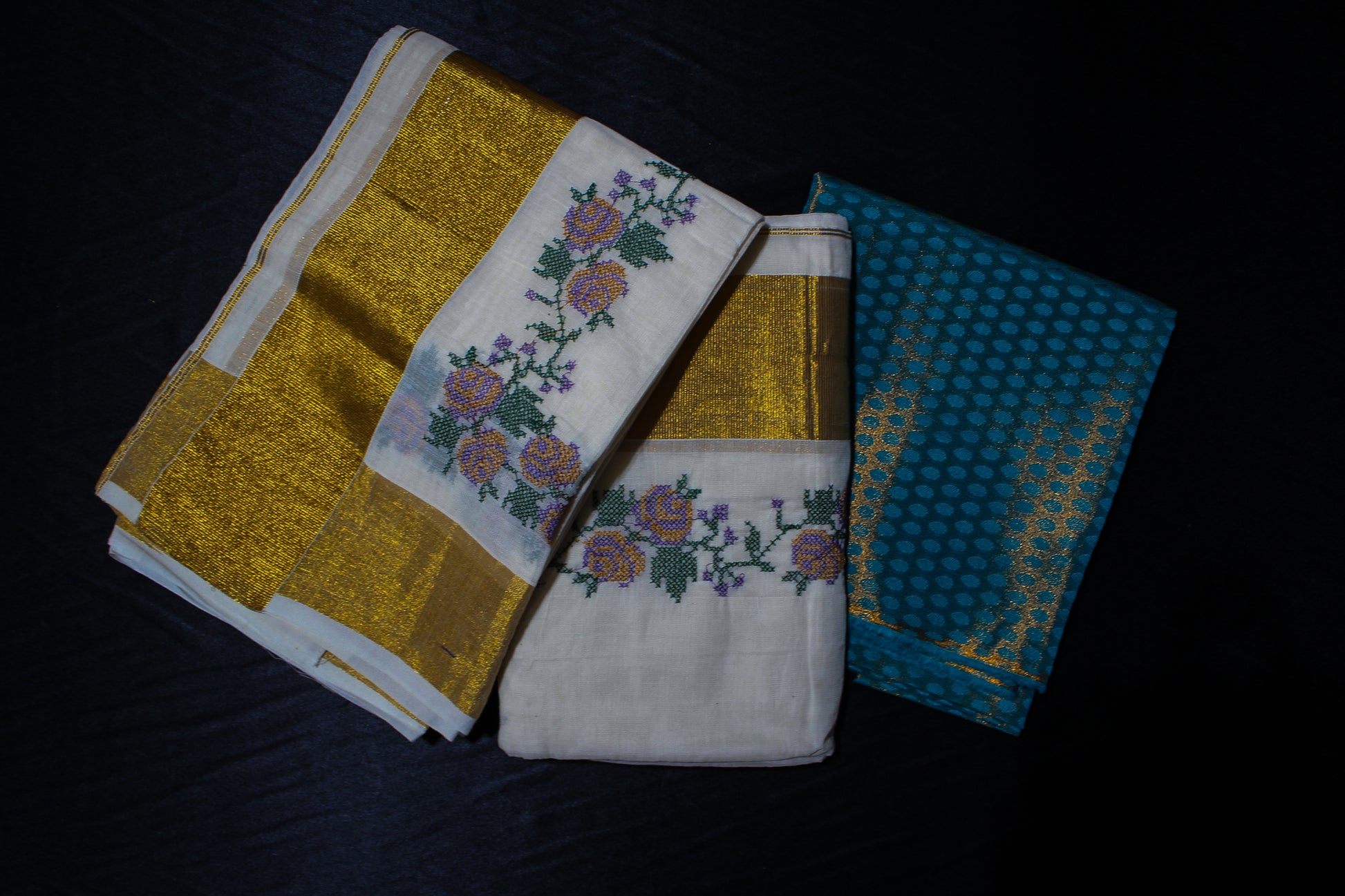 Three embroidered towels in gold, white, and blue on a dark surface